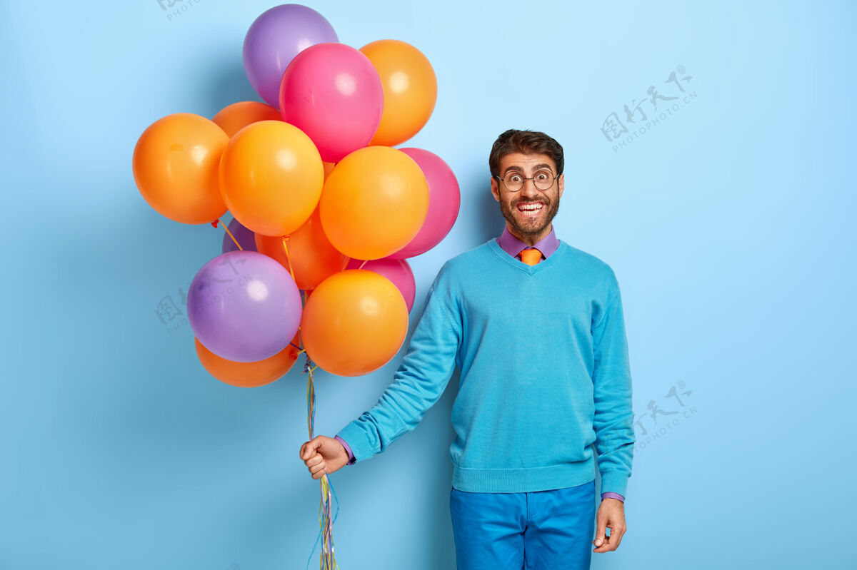 气球戴着生日帽和气球 穿着蓝色毛衣的快乐男人人五颜六色帽子