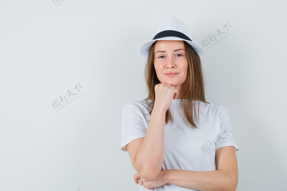 自信年轻女子手托下巴穿着白色t恤 戴着帽子 看上去很自信欢乐帽子女人
