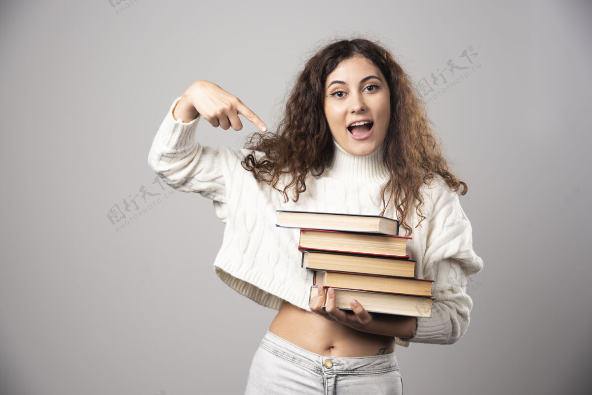 人一位年轻的女士在灰色的墙上展示一堆书高质量的照片女性女士年轻