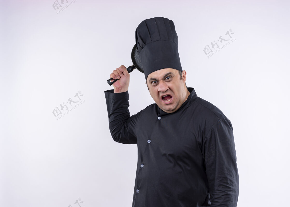 帽子愤怒的男厨师身穿黑色制服 头戴厨师帽 站在白色背景上 挥舞着一个表情咄咄逼人的平底锅烹饪平底锅白