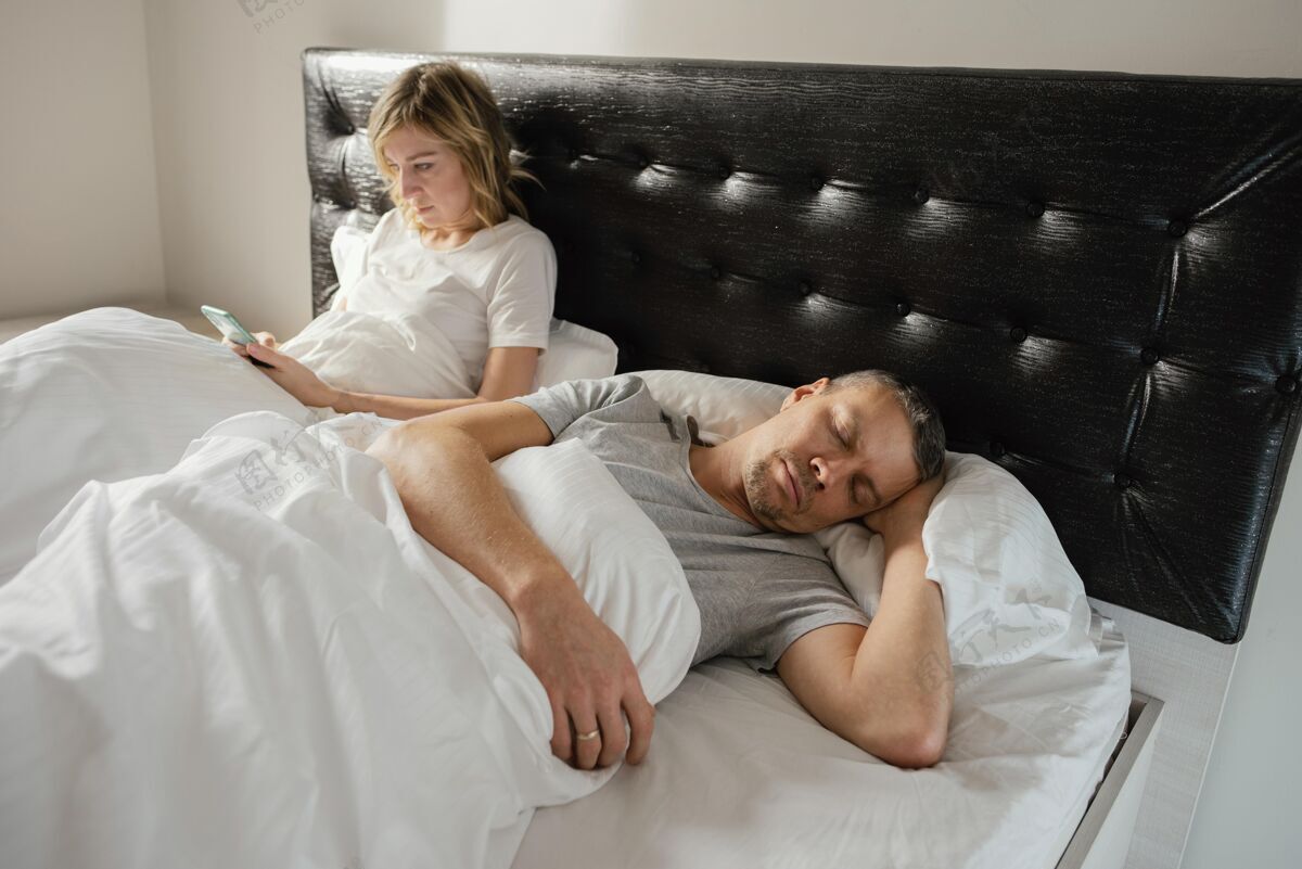 夫妻妻子在丈夫睡觉的时候用手机设备卧室科技