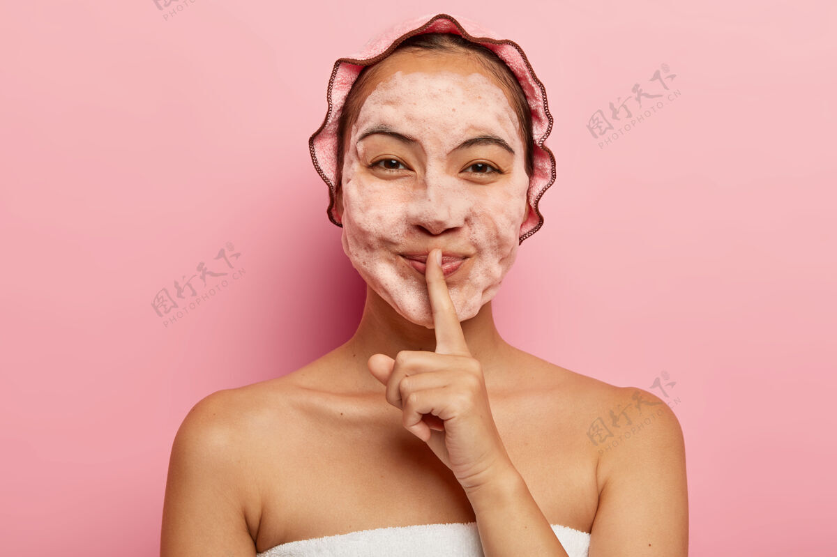 女士美丽的亚洲女士 脸上有泡沫 清洗污垢 要有清爽的表情 做一个沉默的手势 戴上淋浴帽 看起来很开心清洁卫生的概念手势浴室洗澡