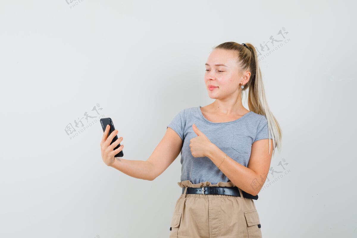 人穿着t恤 裤子的年轻女性在视频聊天中竖起大拇指 看上去很快乐 正面视图黑发年轻时尚