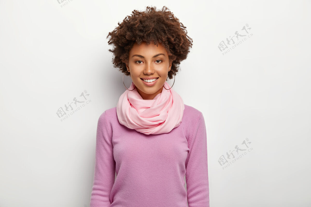 非洲美丽的卷发女人的肖像穿着紫紫色的套头衫和丝巾 看起来笔直 表达良好的情感 模型对白墙人 民族 时尚无忧无虑正面快乐