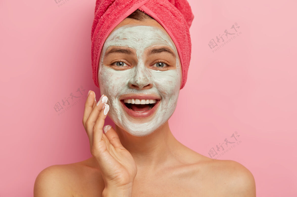 年轻贴近快乐的女性模特画像 用化妆面罩涂抹在她的脸上 有美容法 头上裹着毛巾 焕然一新 更新和治疗柔软微笑姿势