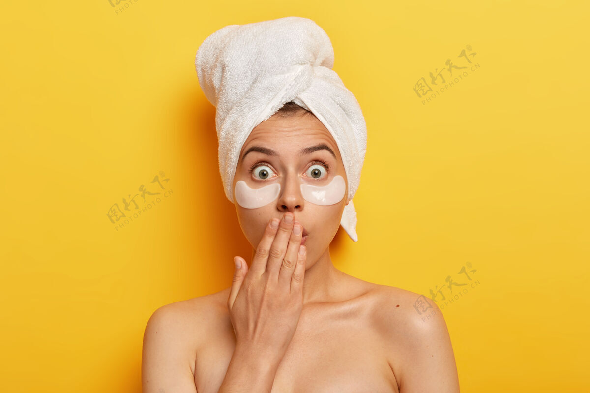 胶原蛋白震惊的水疗女人瞪大了眼睛 被可怕的蜕变吓坏了 用美容贴片滋养眼睛下面的皮肤 头上戴着裹着的毛巾 有抗皱程序 赤身裸体卫生可怕自然