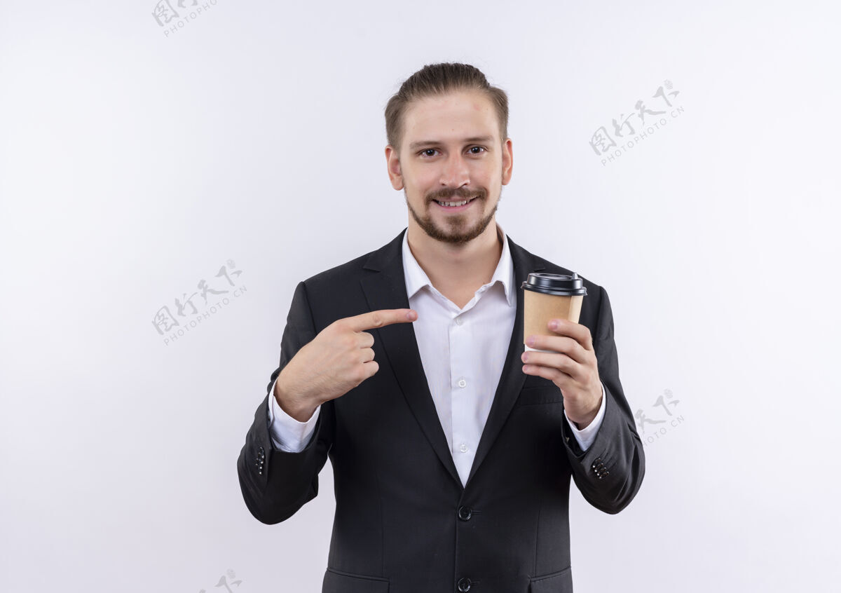 帅气穿着西装的帅哥拿着咖啡杯指着它微笑着站在白色的背景上微笑手指穿着