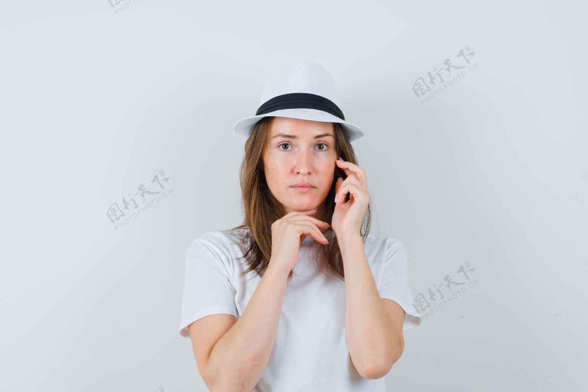 时尚穿着白色t恤的年轻女子 戴着帽子摸着脸上的皮肤 看上去头晕目眩快乐皮肤年轻