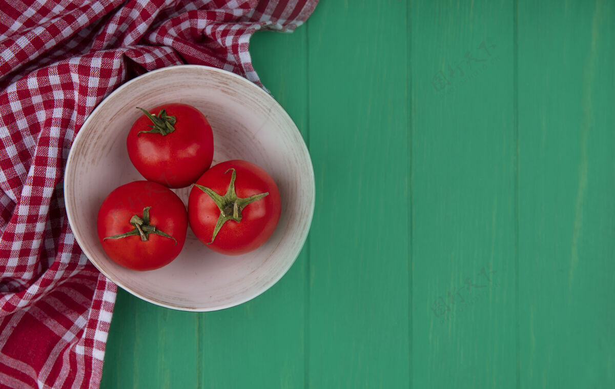 顶部新鲜和红色的西红柿在一个碗上的一个红色格子布上的绿色木制背景与复制空间俯视图蔬菜绿色碗