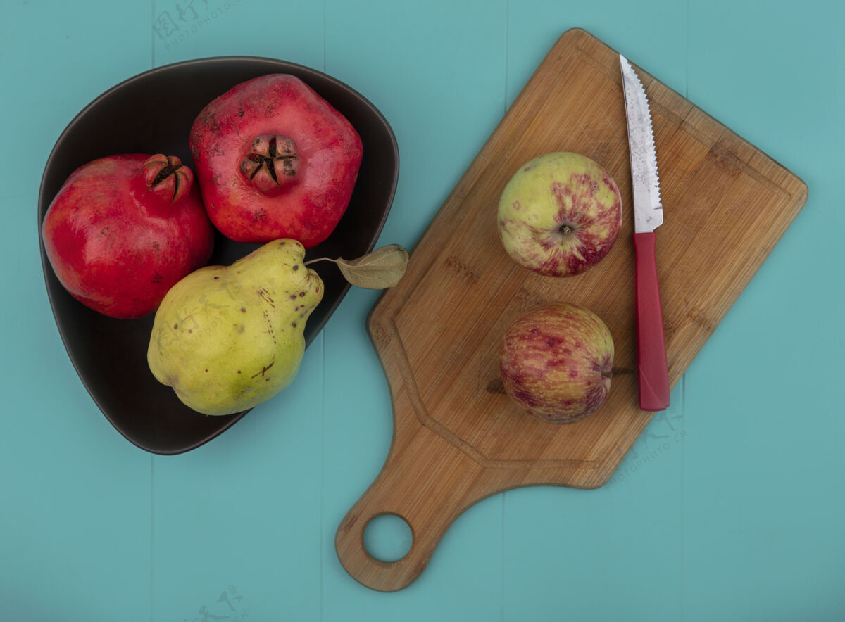苹果红色新鲜石榴的顶视图在一个碗上 苹果放在一个木制的厨房板上 刀子放在蓝色的背景上水果新鲜刀