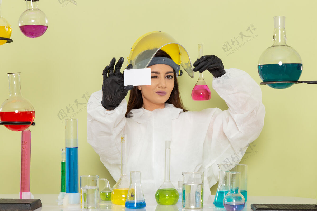 解决方案正面图身着特殊防护服的年轻女化学家手拿绿墙化学实验室化学工作证和溶液女科学医疗前面科学