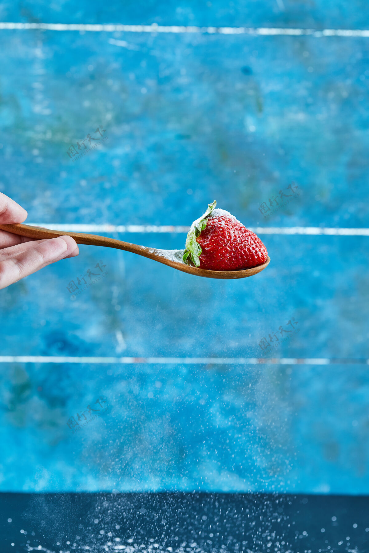 新鲜的在蓝色表面上拿着一勺草莓的女人女人水果叶子