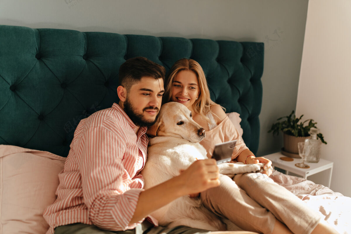 男性一对年轻夫妇和他们的小狗躺在翡翠色的床上的肖像夫妻俩微笑着看着这张难忘的照片拉布拉多房子欢呼