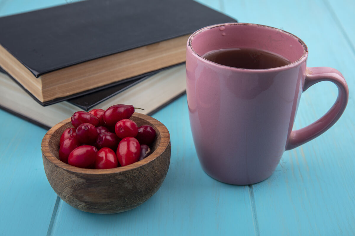 山茱萸新鲜的红色山茱萸浆果在一个木制碗与一杯茶蓝色木制背景俯视图碗红色新鲜