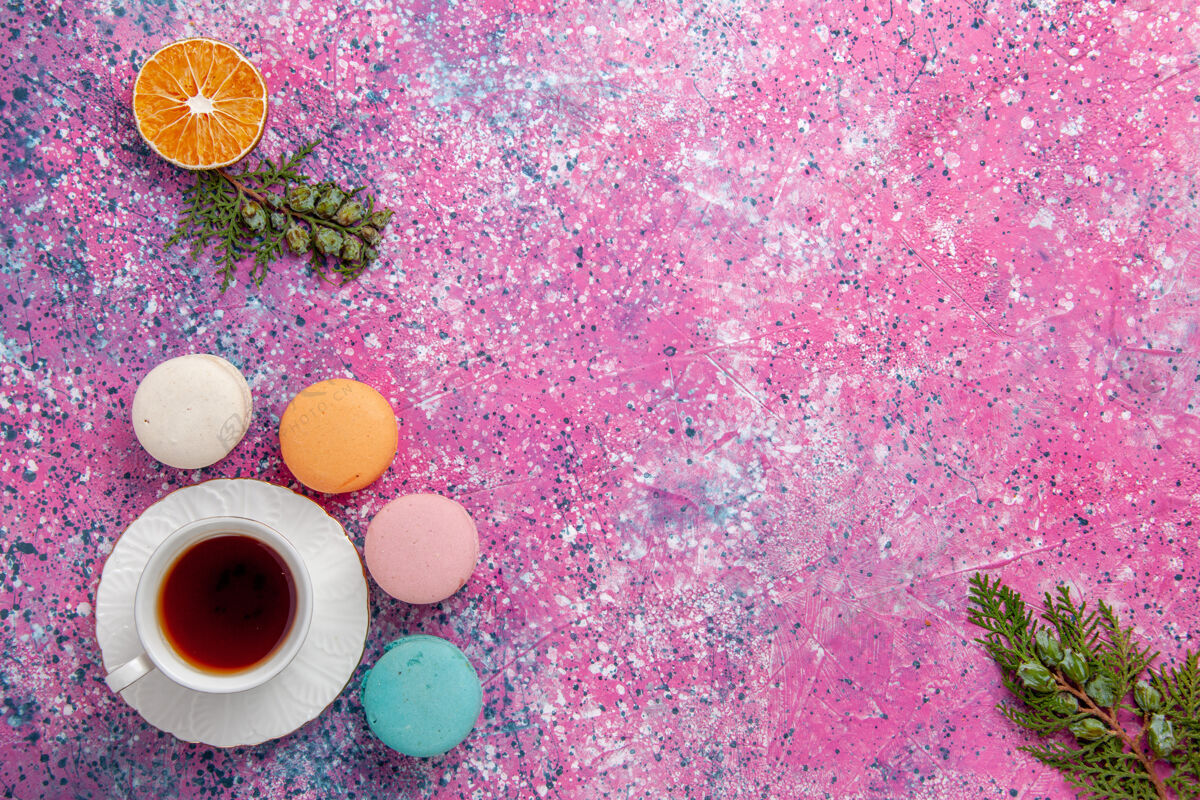 五颜六色顶视一杯茶与法国马卡龙在粉红色的表面杯子生的饮料