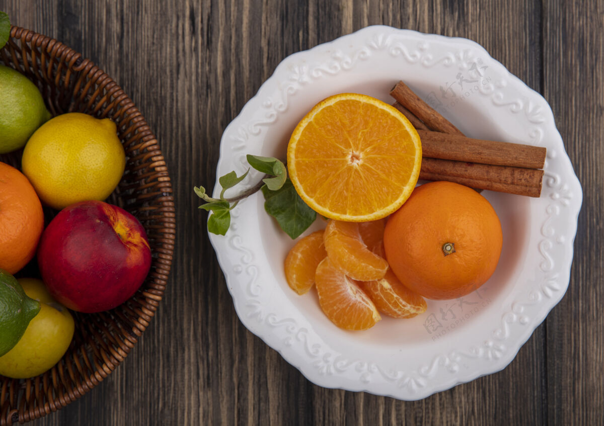 果皮俯视图剥皮的橙色楔形物 肉桂放在盘子里 柠檬 酸橙和桃子放在木制背景的篮子里盘子桃子顶部