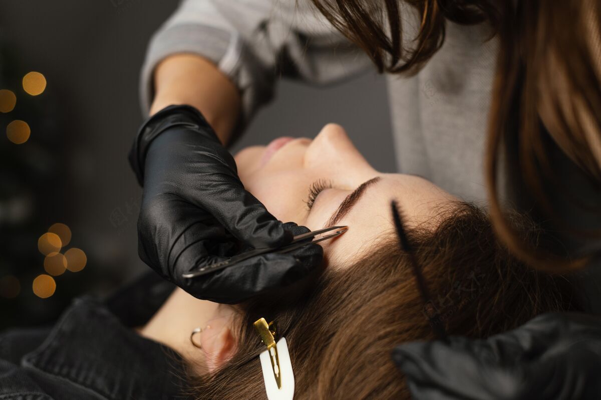 女人女性专家为女性做眉毛治疗的前视图美容乳胶手套镊子