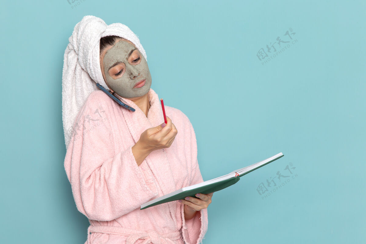 男人正面图身着粉色浴袍的年轻女性在蓝色墙壁上讲电话清洁美容自护霜淋浴专业年轻自我护理