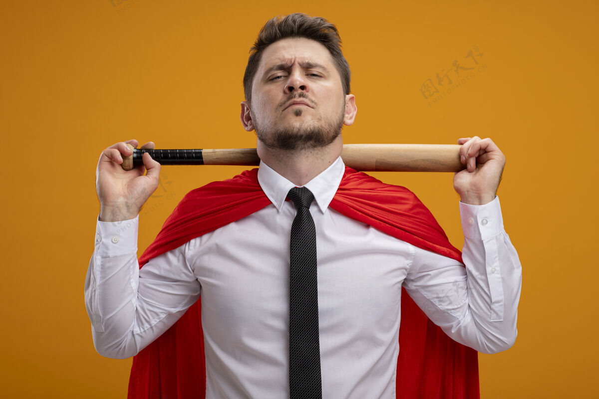 超级穿着红色斗篷的超级英雄商人 脖子后面拿着棒球棒 站在橙色的墙上 看上去很自信蝙蝠超级英雄信心