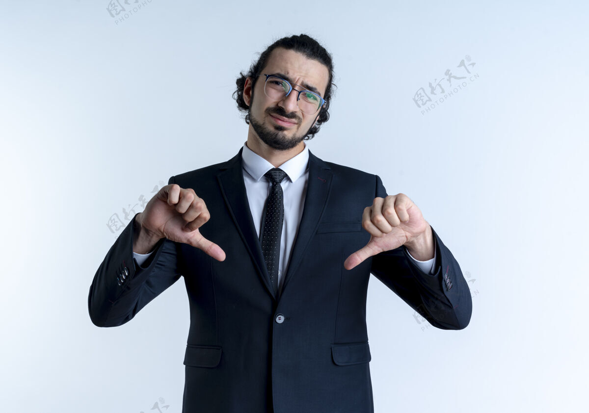 表演一个穿着黑西装戴着眼镜的商人不高兴地站在白墙上竖起大拇指朝前看西装领带优雅