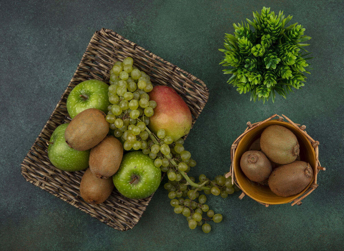 多汁顶视图猕猴桃在一个篮子里与绿色的葡萄苹果和梨子在一个绿色的背景上的立场苹果绿色葡萄
