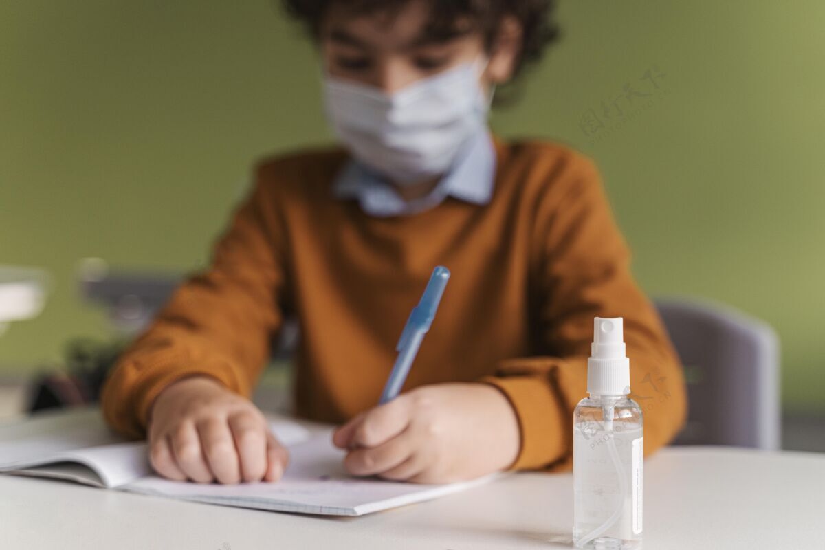 课堂教室里戴着医用口罩的孩子的正面图 桌上放着一瓶洗手液学校病毒冠状病毒