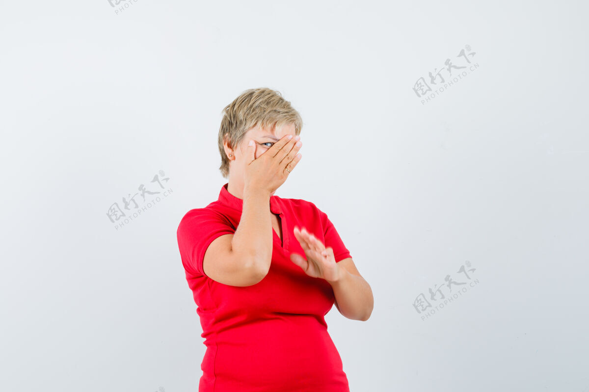 脸穿红色t恤的成熟女人透过手指看 看起来很尴尬可爱白发人
