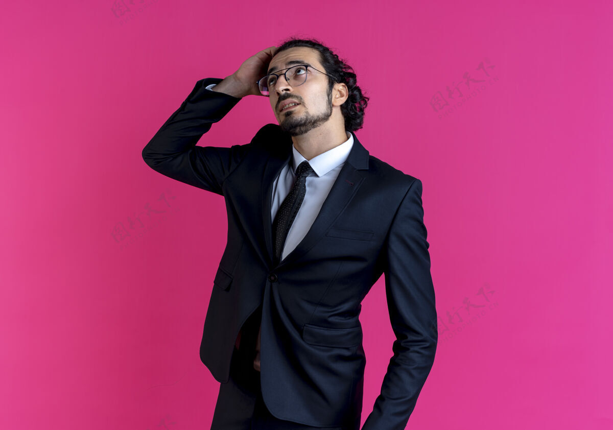 看一个穿着黑西装戴着眼镜的商人站在粉红色的墙上 手放在头上 困惑地抬起头来人站生意