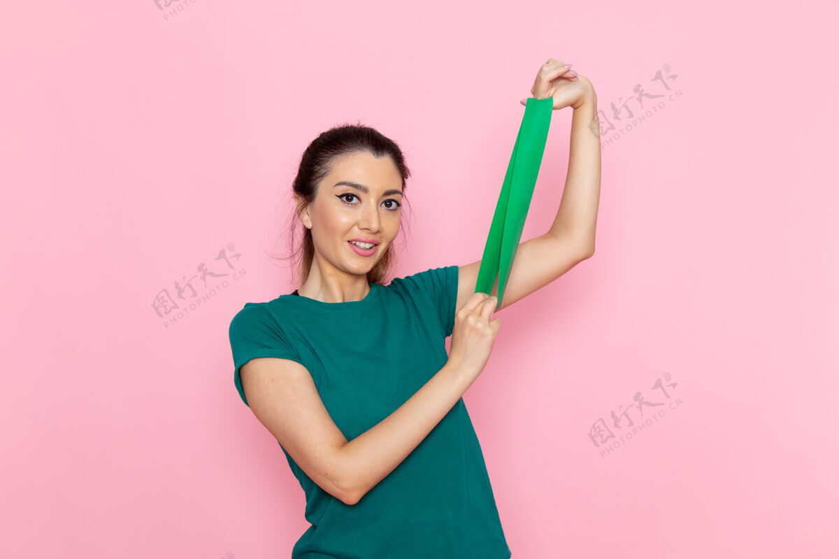 抱着正面图年轻女性拿着绿色绷带在粉红色的墙上美容运动运动员锻炼苗条人微笑欢呼