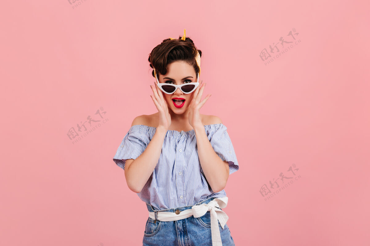 服装一个戴着太阳镜的漂亮女孩一个穿着蓝色条纹衬衫的年轻女子的摄影棚照片女性优雅孤立的粉红色