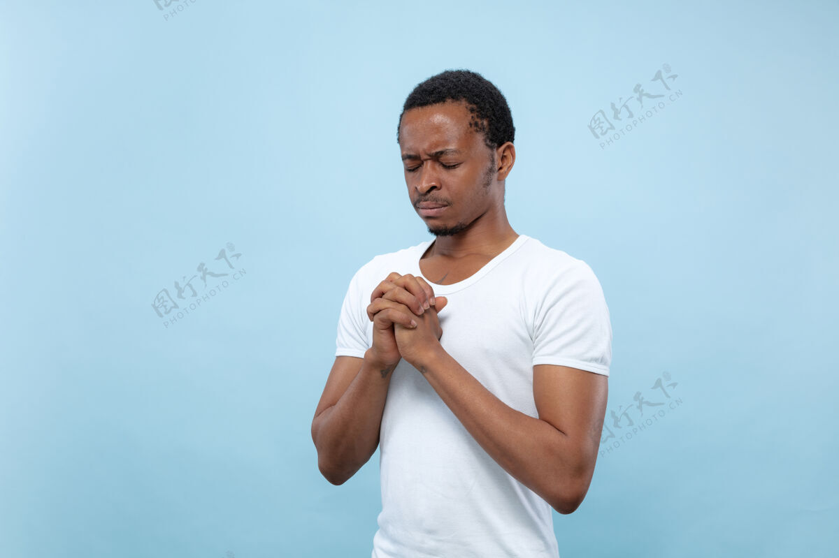商人半身特写 蓝色背景 身穿白衬衫的非洲裔美国青年人类情感 面部表情 广告理念闭上眼睛祈祷 看起来充满希望工作封闭公司