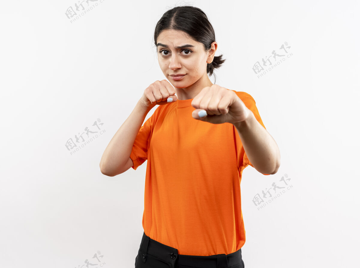 拳击手年轻女孩穿着橙色t恤 握紧拳头 像一个拳击手站在白墙上年轻橙色握紧