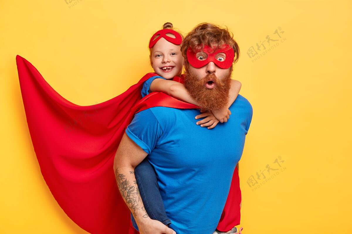 背驮超级英雄团队准备拯救我们的世界小女孩骑在她父亲的超级英雄后面 假装飞行 穿着红色斗篷套装女性拥抱