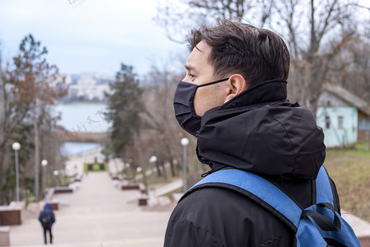 英俊在摩尔多瓦的基希讷乌 一个戴着黑色医用面罩 穿着冬季夹克 背着蓝色背包的男人 以公园为背景细菌户外穿着