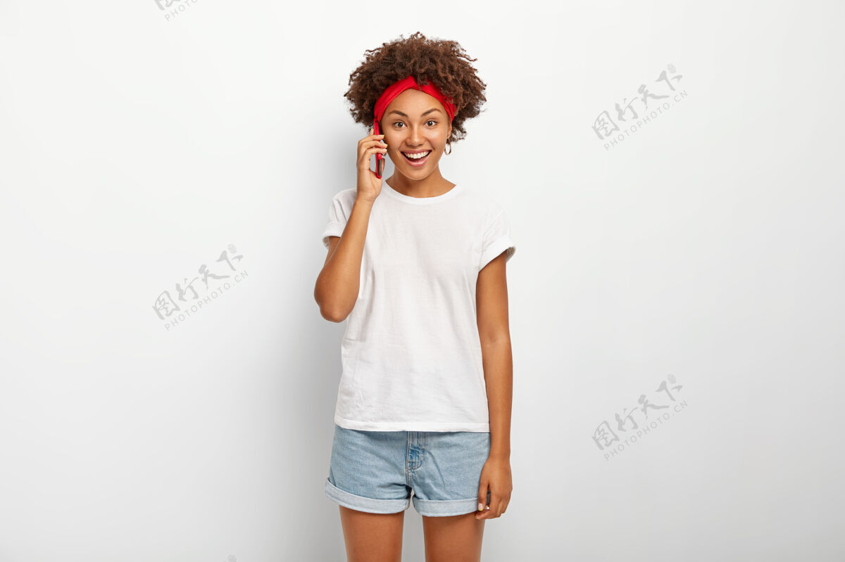 T恤快乐微笑的女人把智能手机放在耳边 与朋友随意交谈 笑容灿烂 露出牙齿听力非洲人表情