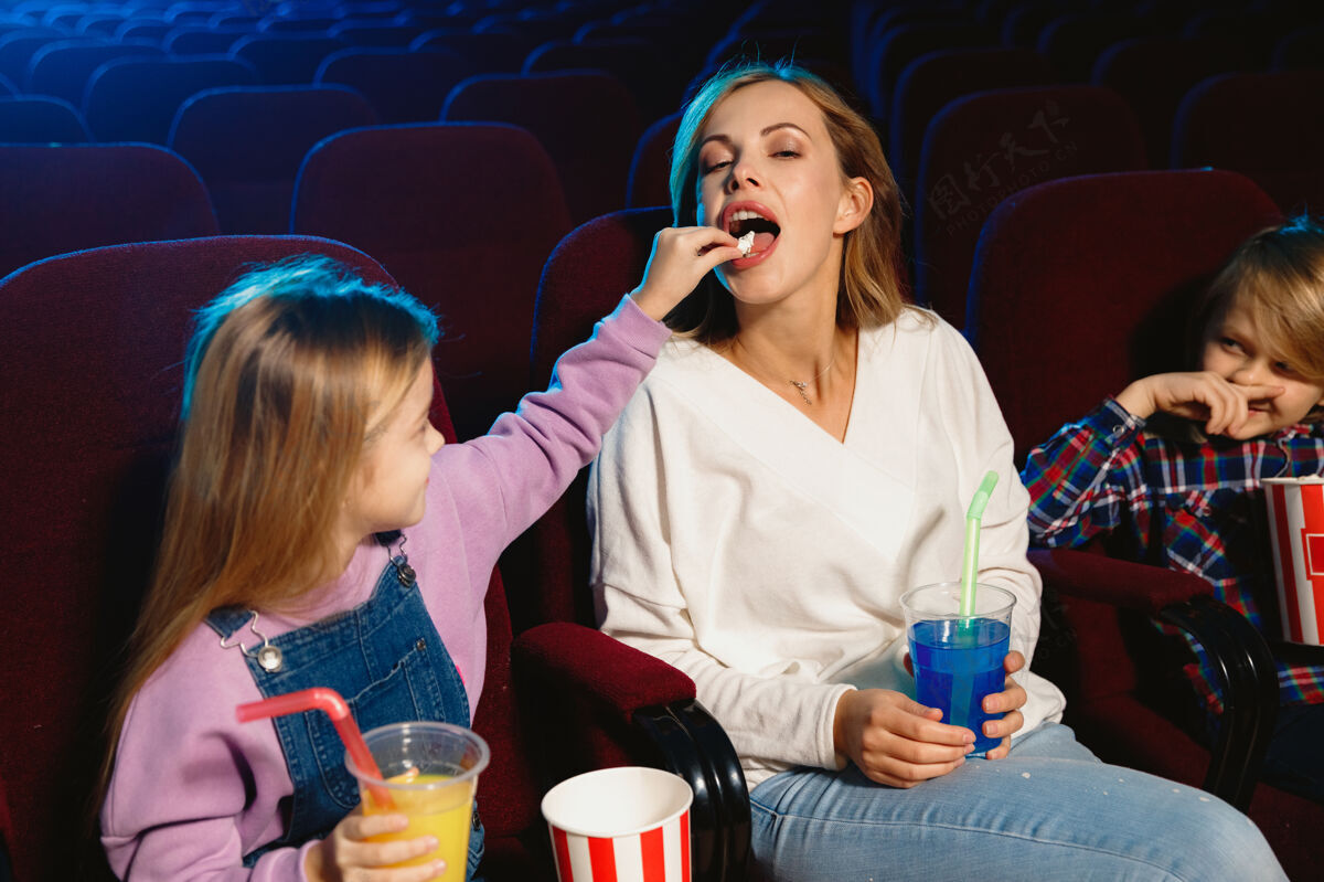 看年轻的白种人家庭在电影院 房子或电影院看电影看起来富有表现力 惊讶和情绪化独自坐着玩关系 爱情 家庭 童年 周末时间金发坐夜生活
