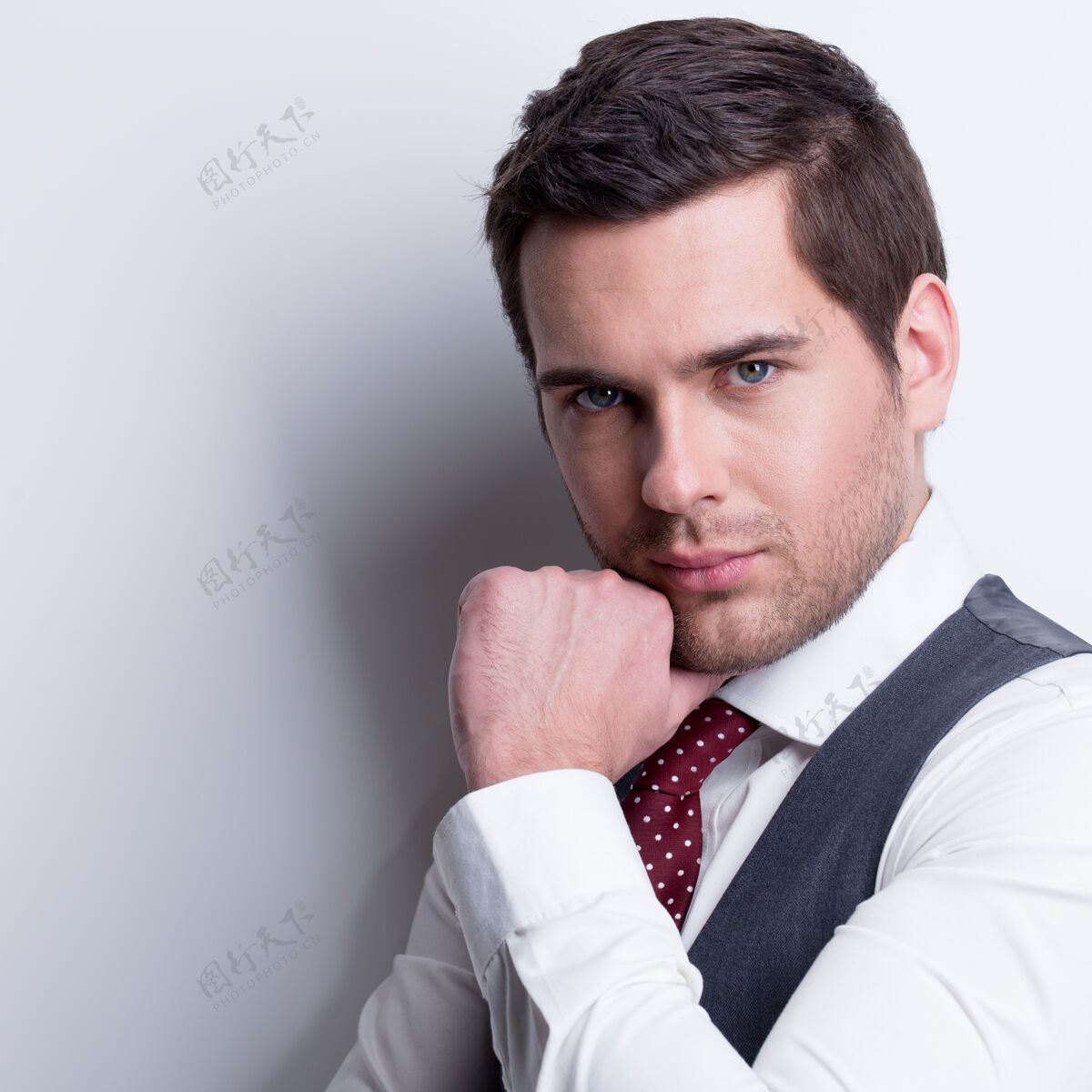 肌肉身着灰色西装 手贴脸的年轻商人的肖像在墙上摆姿势男士成人休闲
