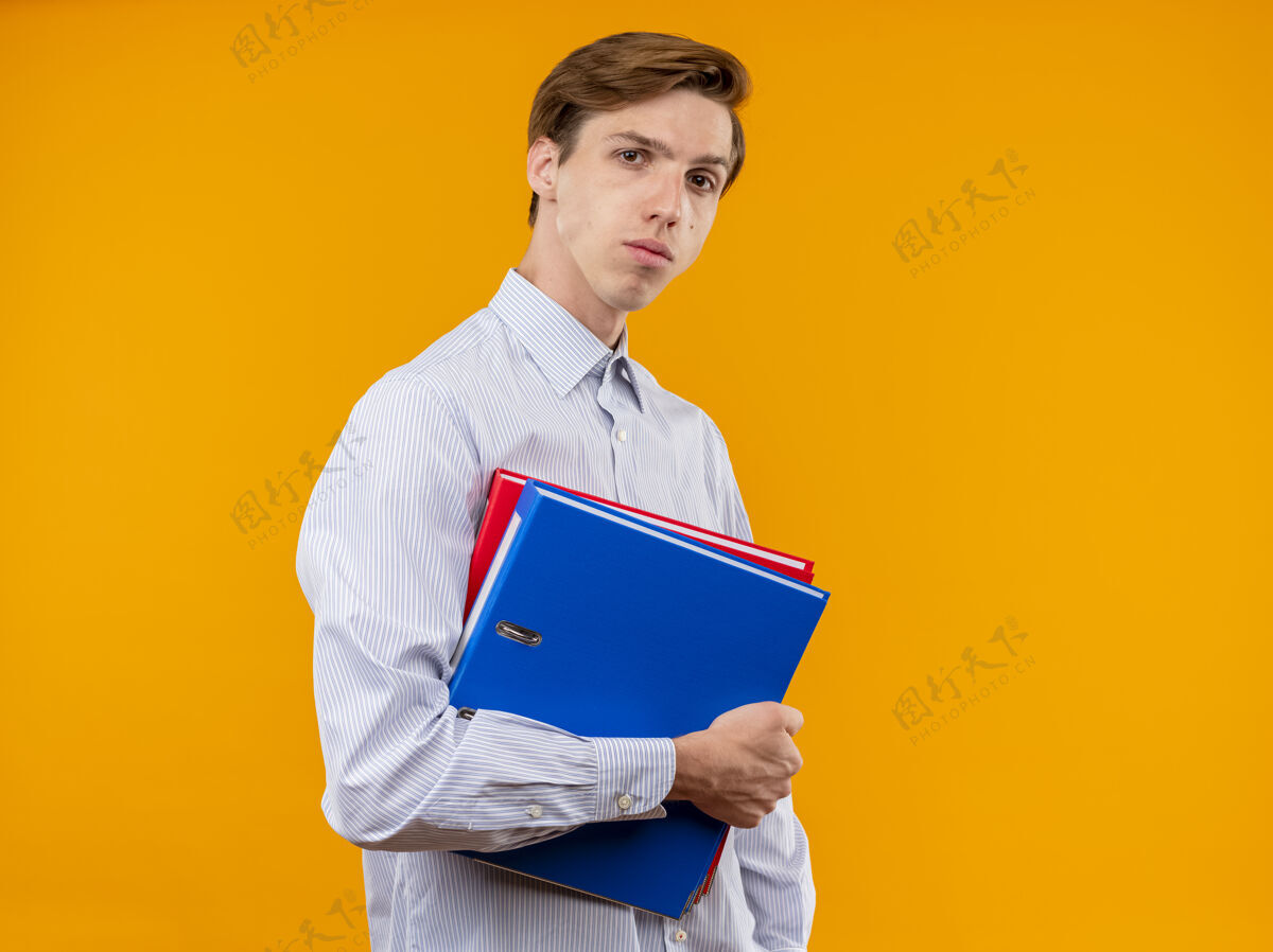 衬衫身穿白衬衫的年轻人拿着文件夹 严肃的脸站在橙色背景下看着摄像机抱着夹着严肃