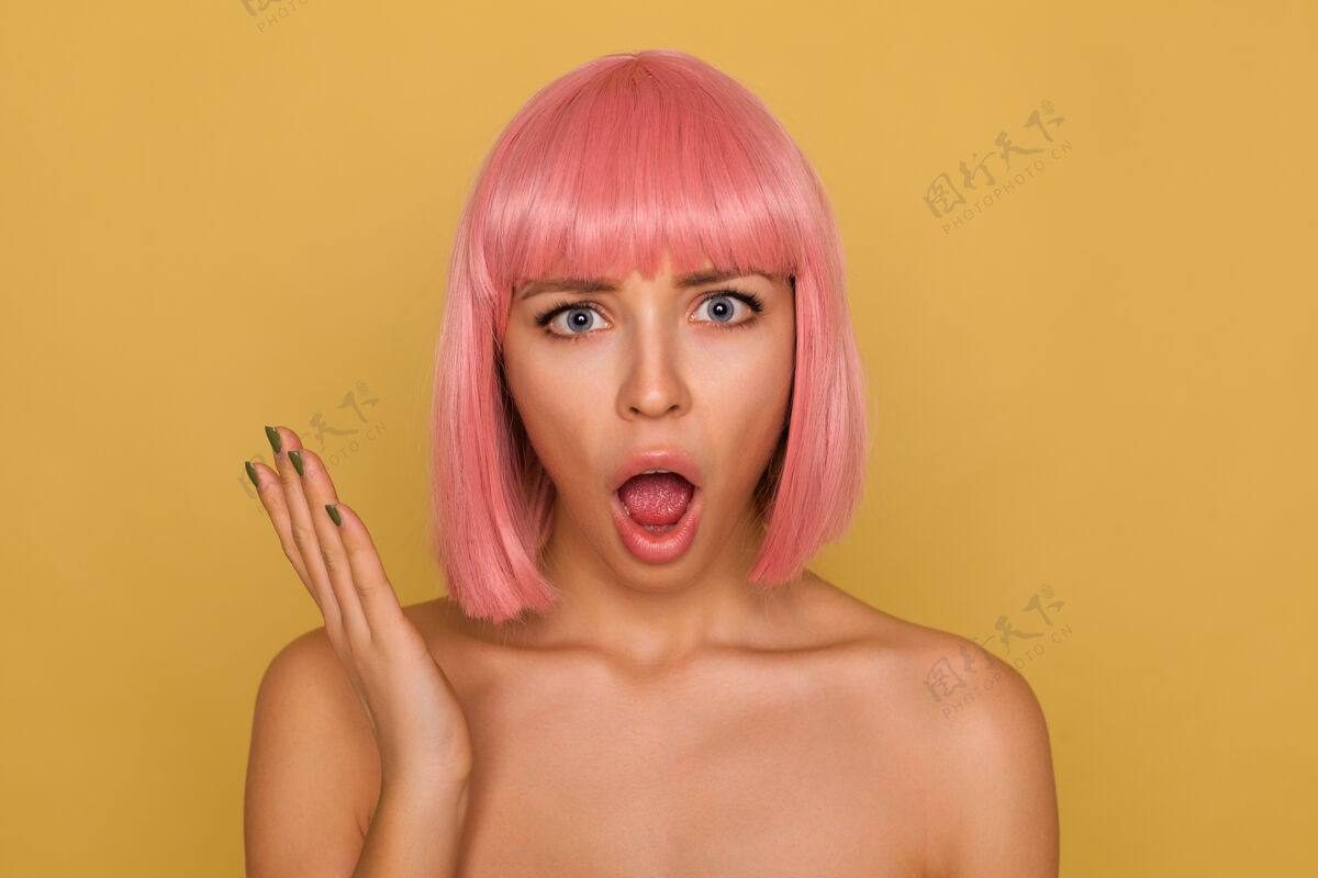 发型愤怒的年轻漂亮的粉红头发女士 自然化妆 情绪化地抬起手掌 张大嘴巴 孤立地看着芥末墙年轻女性休闲