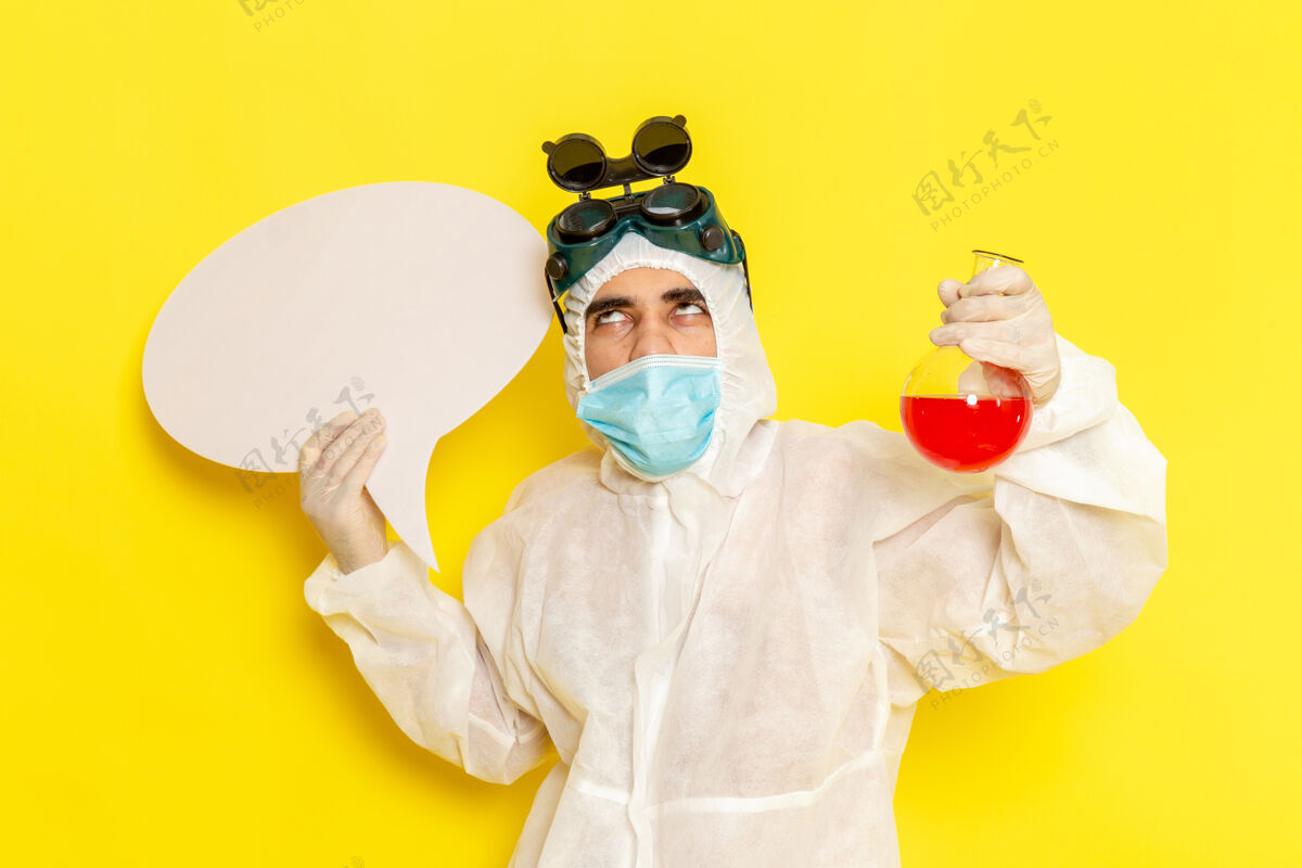 溶液正面图穿着特殊防护服的男科学工作者拿着黄色表面上有红色溶液和白色标志的烧瓶防护正面男性
