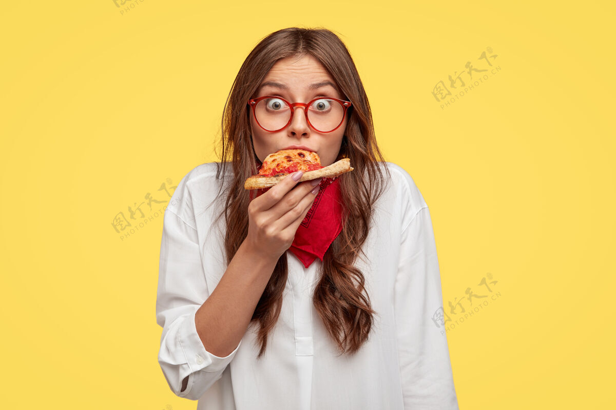 女人惊讶的欧洲时尚女人有一片披萨 看起来穿着超大号衬衫 惊讶的味道很好 隔着黄色的墙人和快餐的概念晚餐凝视反应