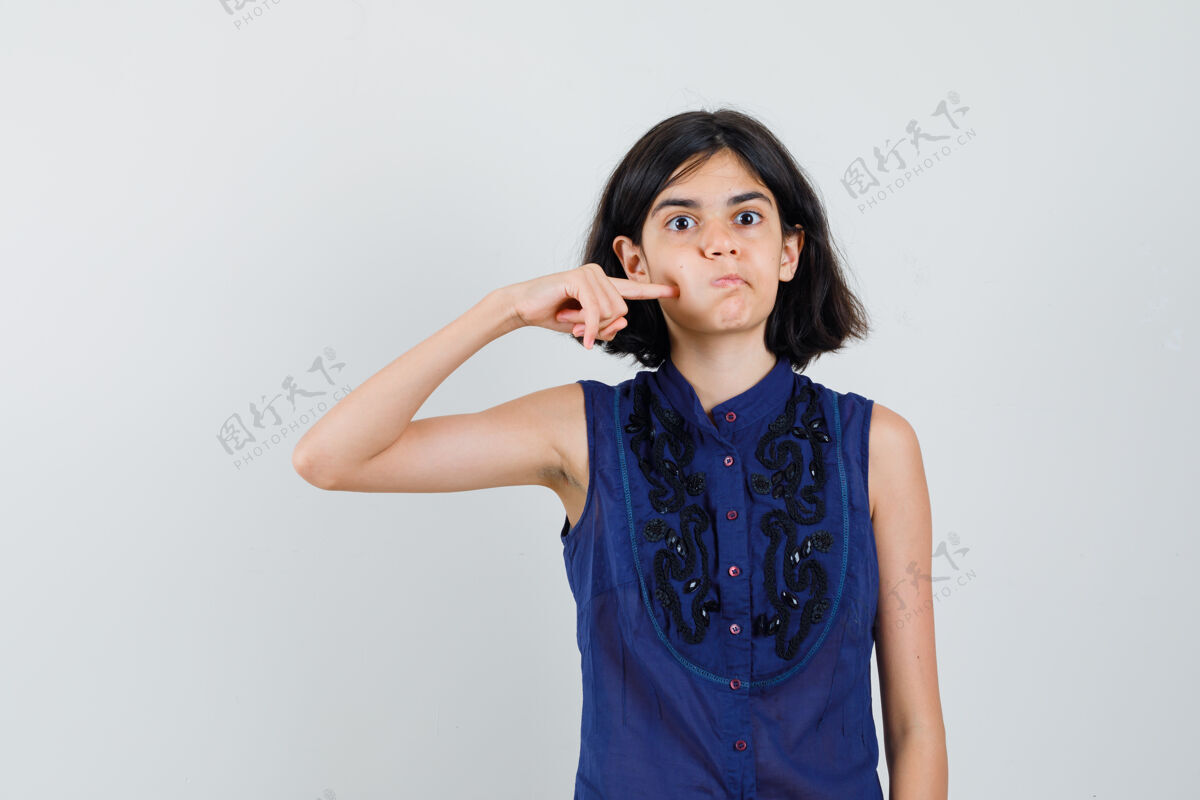 时尚穿着蓝色上衣的小女孩用手指按着吹坏的脸颊 看上去很滑稽女性休闲小
