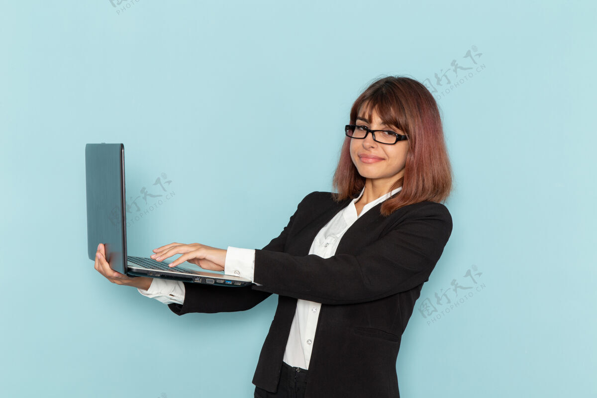 严格正面图身着西装的女上班族微笑着在蓝色表面上使用笔记本电脑使用前台办公室