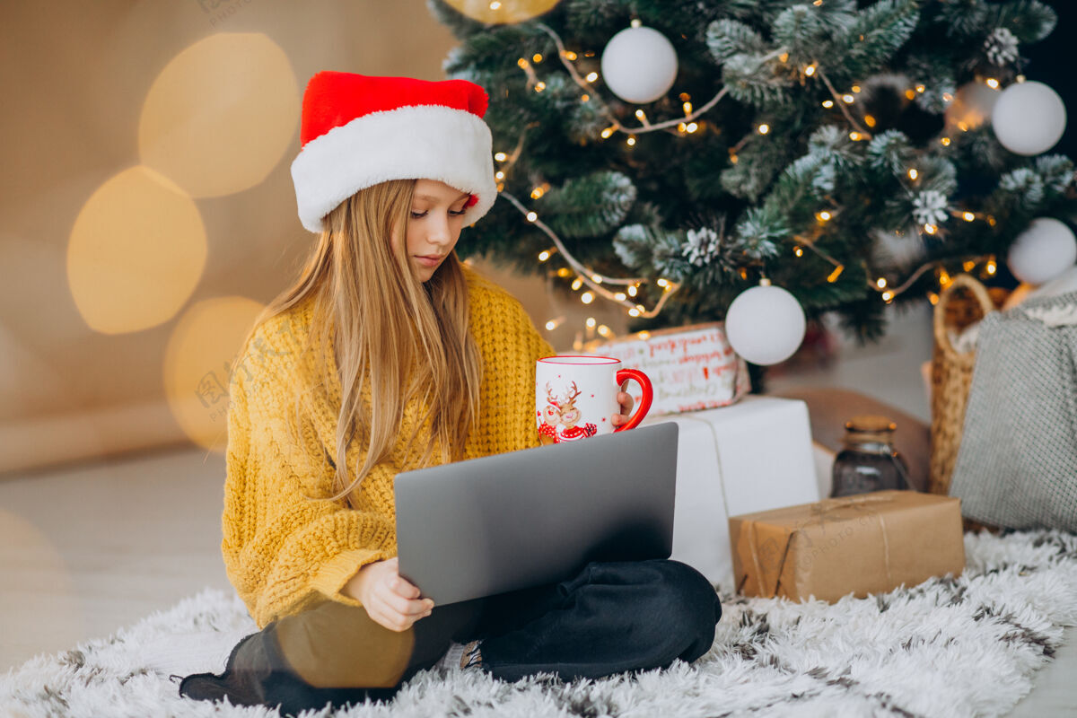 笔记本电脑可爱的女孩在圣诞树旁用电脑圣诞圣诞树庆祝