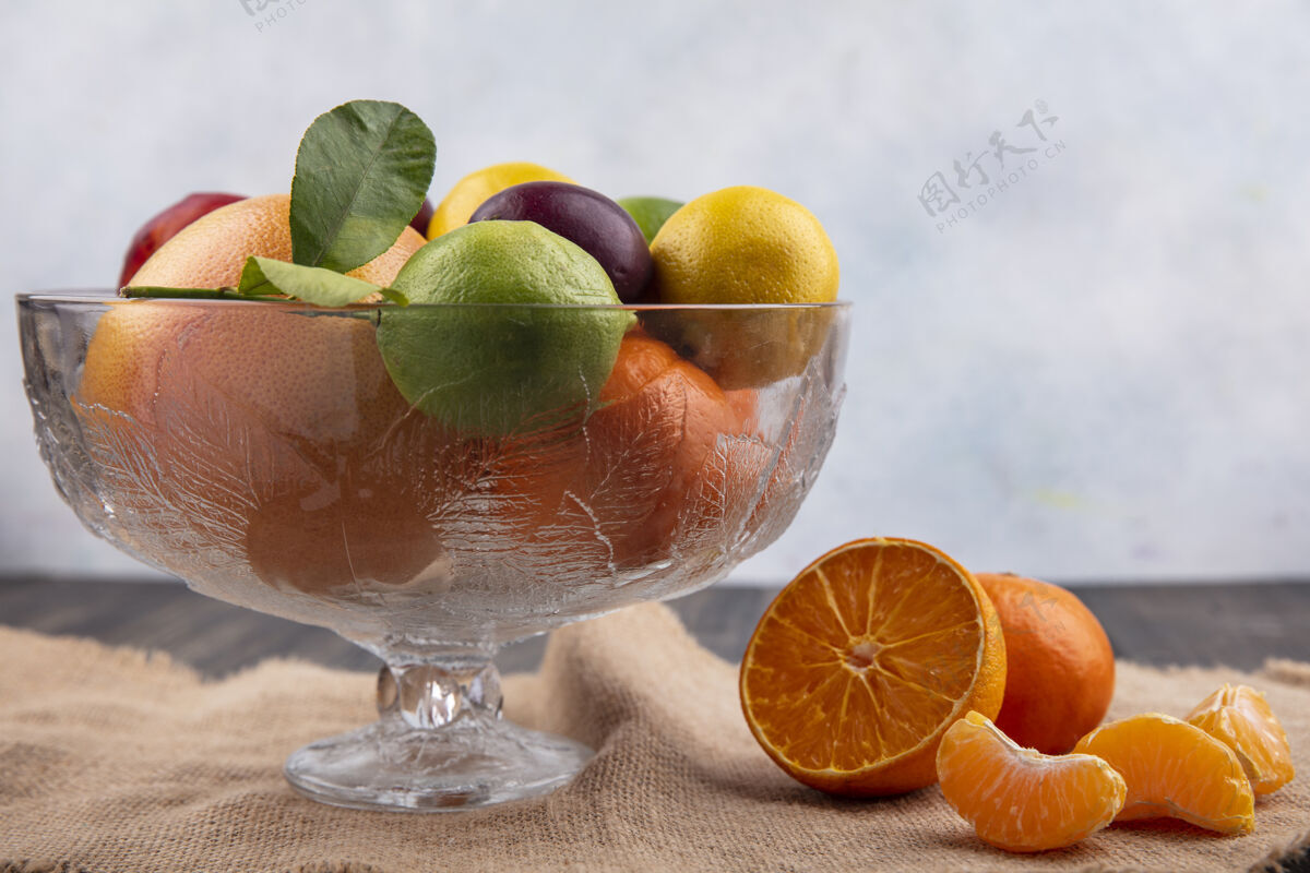 橙色前视图混合水果柠檬柠檬李子桃子和橘子在一个花瓶米色餐巾混合新鲜正面