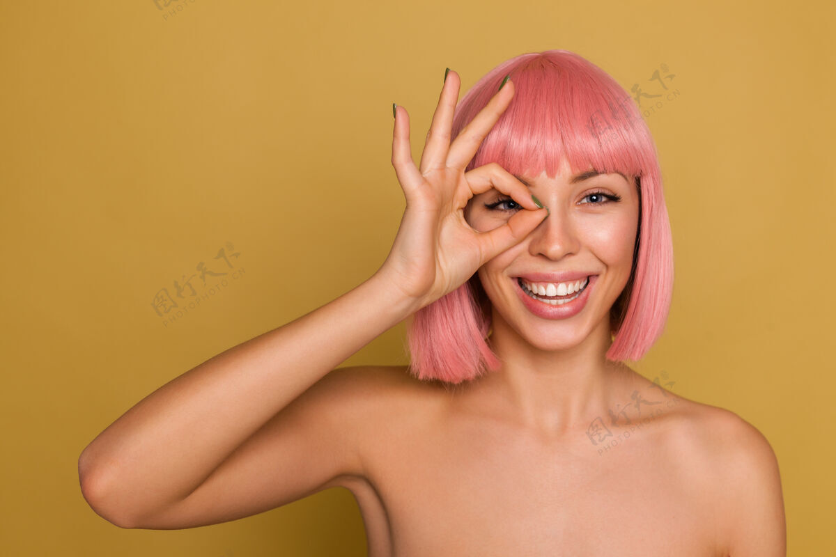鲍勃快乐迷人的年轻蓝眼睛粉红色头发的女性 鲍勃的发型精神饱满 微笑愉快地站在芥末墙上升起的ok标志动画可爱女性