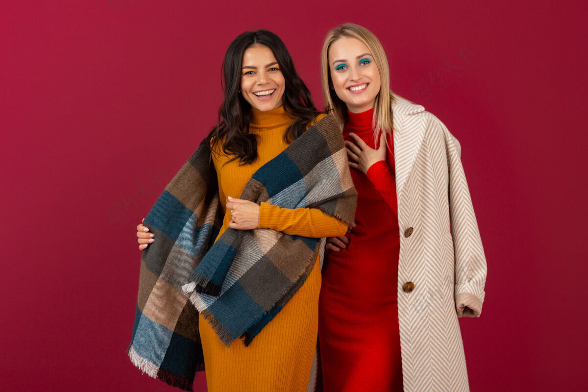 夹克两位笑容可掬的时尚女性穿着秋冬时装和外套 在红墙上孤零零地摆着姿势外套颜色姿势