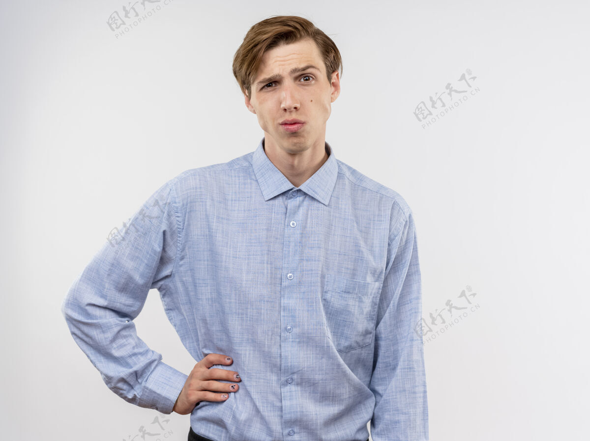 臀部身穿蓝色衬衫的年轻人看着相机 手放在臀部 站在白色背景上 表情诡异衬衫年轻表情