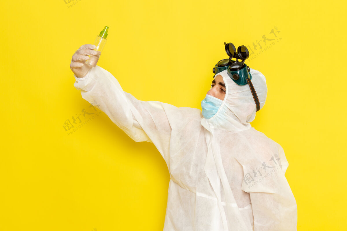 喷雾正面图身着特殊防护服的男科学工作者拿着喷雾瓶站在黄色的桌子上服装化学特殊