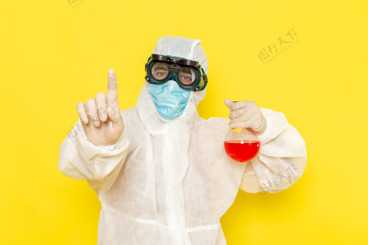 正面正面图穿着特殊防护服的男科学工作者拿着浅黄色表面上有红色溶液的烧瓶科学烧瓶防护